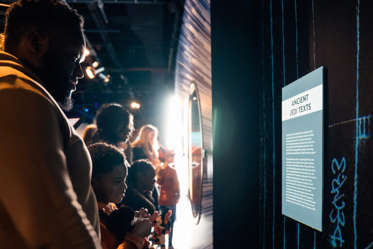 A family looking at the ancient jedi texts at the Disney100: The Exhibition